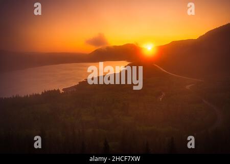 Die Sonne ragt während des Sonnenaufgangs knapp über den kanadischen Rockies hoch, während sich der Nebel über dem See bewegte. Stockfoto