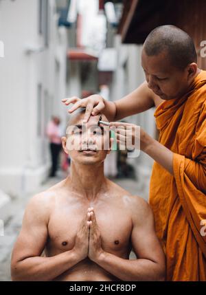 Das Nahaufnahme-Bild eines hübschen asiatischen Mannes rasiert die Haare vom Kopf eines Mannes, der im Buddhismus ordiniert ist. Stockfoto