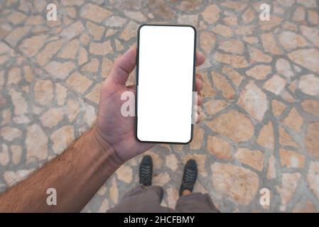 Fußgänger-Mann mit Handy-Smartphone mit leerem Mockup-Bildschirm auf der Straße, über Kopf geschossen mit selektivem Fokus Stockfoto