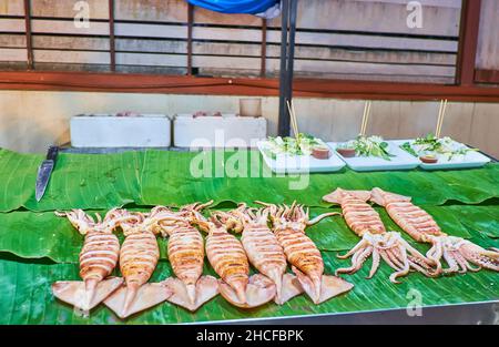 Die gegrillten Tintenfische auf grünen Bananenblättern auf der Theke des Street Food Stalls, Saturday Night Market, Chiang Mai, Thailand Stockfoto