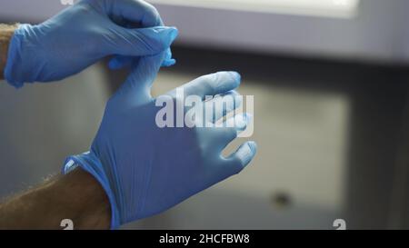 Schutz vor ansteckenden Krankheiten, Coronavirus, Mann trägt hygienische Handschuhe, um Infektionen zu verhindern. Nahaufnahme von Menschenhänden, die schützendes Blau aufziehen Stockfoto