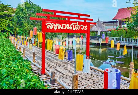 Das leuchtend rote Holztor am Eingang zur alten Bambusbrücke auf dem See, bedeckt mit Lotusgrün, Wat Jedlin, Chiang Mai, Thailand Stockfoto