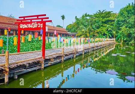 Das rote dekorative Holztor und der Bambussteg auf dem Teich mit Lotusblumen und Seerosen im Park des Wat Chetlin (Jedlin, Jetlin)-Tempels, Chiang Mai, Stockfoto