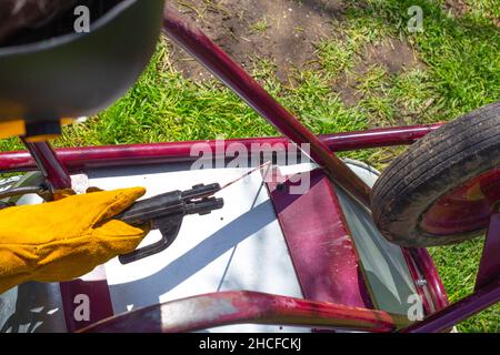 Der Mann arbeitet durch Schweißen. Ein Schweißer repariert einen eisernen Gartenwagen mit Elektroschweißen. Stockfoto