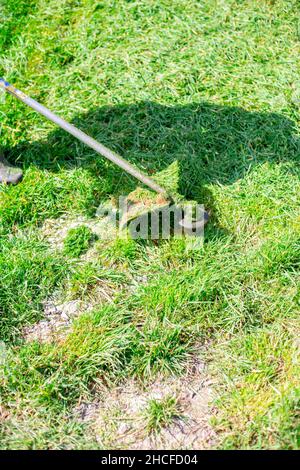 Ein Mann mäht junges grünes Gras mit einem Benzinmäher und einem Trimer. Pflegen des vorderen Rasens Stockfoto