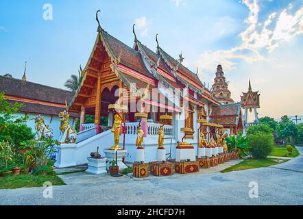 Das malerische grüne Gelände des Wat Puak Hom Tempels mit seinem verzierten Viharn, umgeben von goldenen Skulpturen von Buddha und Mönchen, Chiang Mai, Thailand Stockfoto