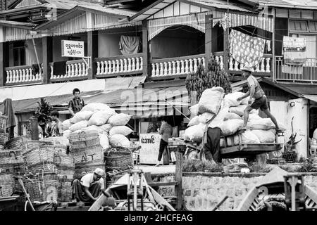 Burmesische Männer laden und entladen Säcke mit Vorräten und Lebensmitteln von Booten zu Karren, in Inle Lake Stockfoto