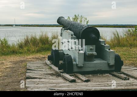 Eine historische Kanone aus schwarzem Metall mit Blick auf einen Fluss auf St. Simon's Island, Georgia, tagsüber im Fort Frederica. Stockfoto