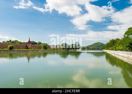 Ein großer, reflektierender Wasserpool, mit einem entfernten Blick auf den Mandalay-Hügel, gegen den blauen und bewölkten Himmel Stockfoto