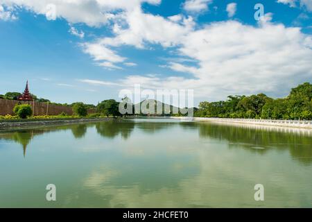 Ein großer, reflektierender Wasserpool, mit einem entfernten Blick auf den Mandalay-Hügel, gegen den blauen und bewölkten Himmel Stockfoto