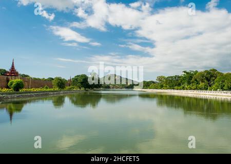 Ein großer, reflektierender Wasserpool, mit einem entfernten Blick auf den Mandalay-Hügel, gegen den blauen und bewölkten Himmel Stockfoto