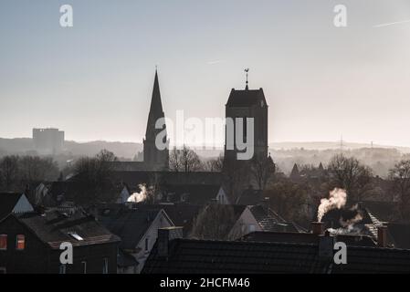 Blick über die Dächer von Bochum Langendreer in Deutschland mit den beiden Kirchen und dem Universitätsklinikum im nebligen Hintergrund. Rauchenden Kaminen. Stockfoto
