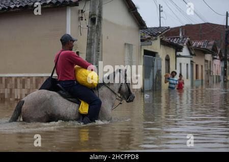 Bahia State, Brasilien. 28th Dez 2021. Am 28. Dezember 2021 reitet ein Mann auf einer wasserverlaufenden Straße auf einem Pferd, während die Überschwemmungen durch starke Regenfälle in der Stadt Dario Meira, Bundesstaat Bahia, Brasilien, verursacht wurden. Laut einem Bericht der Zivilschutzbehörden des Bundesstaates Bahia stieg die Zahl der Todesopfer durch schwere Regenfälle, die den nordöstlichen brasilianischen Bundesstaat Bahia heimgesucht haben, am Montag auf 20 an, wobei 358 Menschen verletzt wurden. Nach Angaben des Nationalen Instituts für Meteorologie wird sich die hohe Regenmenge, die das südliche Bahia seit November verwüstet hat, diese Woche fortsetzen und bis in den Januar hinein ausdehnen. Quelle: Xinhua/Alamy Live News Stockfoto