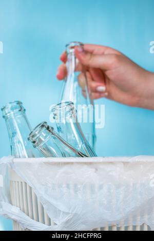 Hand hält eine Glasflasche in einem Recycling-Behälter, der einen weißen Beutel auf hellblauem Hintergrund hat Stockfoto