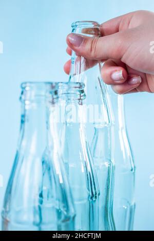 Kaukasische Hand, die eine Glasflasche mit hellblauem Hintergrund nimmt Stockfoto