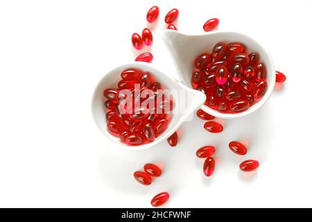 Krillöl rote Gelatinekapseln in weißen Keramikbechern auf weißem Hintergrund.Omega-Fettsäuren.gesunde Ernährung und Nahrungsergänzungsmittel Stockfoto