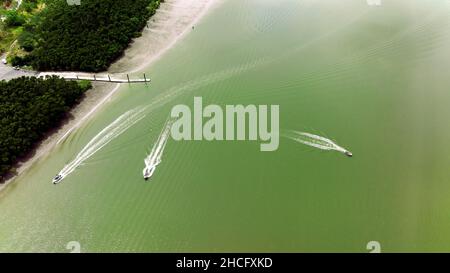 Drei Motorboote, die von der Bootsrampe und dem Anlegesteg von Conway Beach auf dem Weg zum Gezeitenbach abfahren Stockfoto