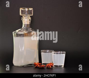 Anislikör, starker selbstgemachter Alkohol in einer Glasflasche und zwei Gläser auf schwarzem Hintergrund. Nahaufnahme. Stockfoto
