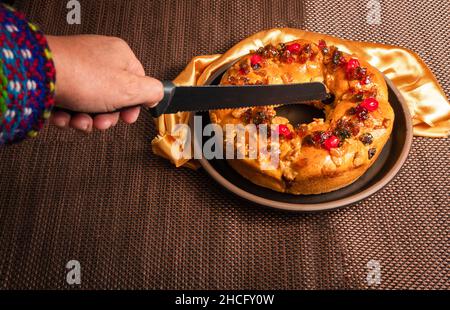 Die Hand eines Mannes, der mit einem Messer einen Roscon de reyes schneidet Stockfoto