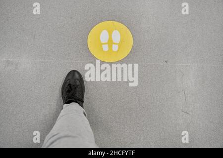 Der Mann in schwarzen Schuhen und weißen Hosen folgt den Schildern auf dem Boden des Einkaufszentrums Stockfoto