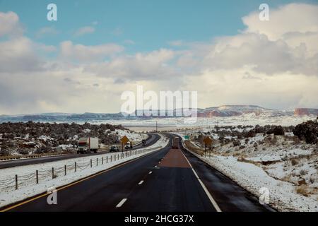 Die schneebedeckte rote Felsenkette hinter der Wüstenlandschaft entlang der I-40 Autobahn in New Mexico Stockfoto