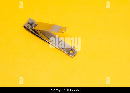 Ein offener grauer Nagelschneider auf dem gelben Hintergrund mit schrägem Schuss Stockfoto