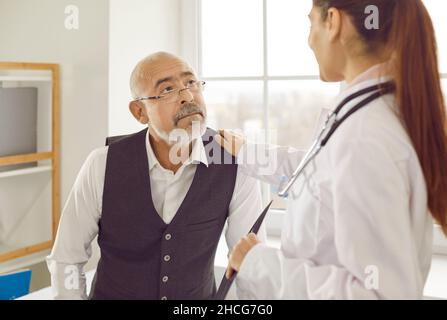 Der Arzt legt ihre Hand auf die Schulter ihres älteren Patienten, um ihn zu beruhigen und zu unterstützen Stockfoto