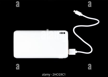 Weiße Powerbank zum Aufladen von Smartphones und verschiedenen digitalen Geräten auf schwarzem Hintergrund, Nahaufnahme von oben Stockfoto