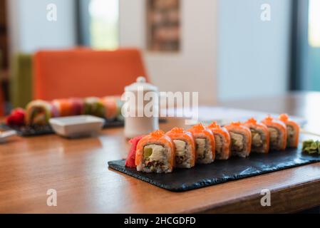 Selektiver Fokus des Tellers mit Sushi-Rollen in der Nähe von Sojasauce-Topf und Schüssel auf verschwommenem Hintergrund Stockfoto