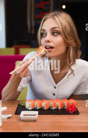 Junge blonde Frau, die köstliche Brötchen in der Sushi-Bar isst Stockfoto