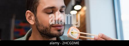 Junger Mann mit Essstäbchen mit köstlicher Sushi-Rolle, Banner Stockfoto