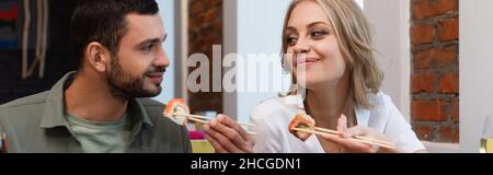 Glückliches Paar, das sich ansieht, während es köstliche Sushi-Brötchen und Banner isst Stockfoto