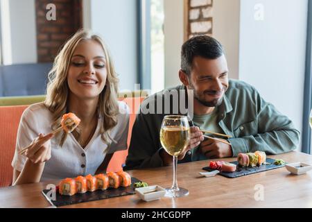 Fröhlicher Mann mit geschlossenen Augen, der Sushi in der Nähe einer lächelnden Freundin im Restaurant isst Stockfoto