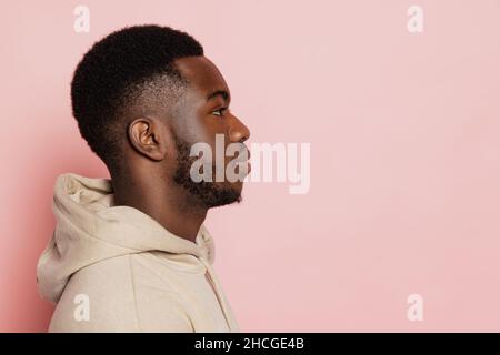 Profilansicht des jungen ernsthaften dunkelhäutigen Mannes schaut gerade nach vorne isoliert auf rosa Studio-Hintergrund mit Copyspace für Anzeige. Stockfoto