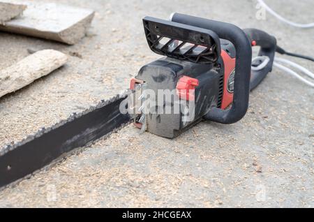 Die schwarze Hand-Stromsäge liegt in der Nähe des Brennholzes Stockfoto