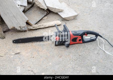 Die schwarze Hand-Stromsäge liegt in der Nähe des Brennholzes Stockfoto