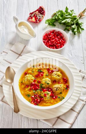 Ash-e Anar, iranische gelbe, geteilte Erbse Granatapfelsuppe mit Fleischbällchen, dicke Suppe, in einer weißen Schüssel auf einem strukturierten weißen Holztisch mit Zutaten und Stockfoto