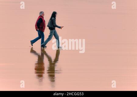 Abendlicht über Urlauber, die bei Ebbe am Fistral Beach in Newquay in Cornwall spazieren. Stockfoto