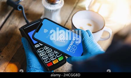Kontaktieren Sie weniger Zahlung auf einem Mobiltelefon. Nahaufnahme einer Frauenhand mit Handschuhen, die kontaktlos mit einer Smartphone-Bildschirm-Anwendung bezahlen. Stockfoto