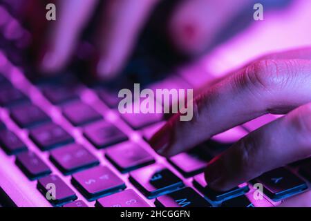 Nahaufnahme Frau Hände tippen auf Laptop-Tastatur, professionelle Online-Gamer Finger auf Notebook-Tastatur in Neon-Farbe, sitzen am Gaming-Schreibtisch Stockfoto