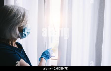 Ängstliche ältere Frau in Corona COVID-19 Quarantäne, die aus dem Fenster auf die Straße schaut Stockfoto