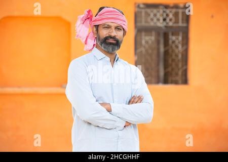 Porträt eines selbstbewussten indischen Bauern, der traditionelle Kurta trägt und ein Tuch um seinen Kopf herum trägt und einen Kreuzarm steht. Bartmann Nahaufnahme beim Blick auf die Kamera. Ländlich Stockfoto