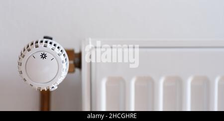 Thermostatisches Heizkörperventil auf niedrige Temperatur an einer weißen Wand eingestellt, mit Copyspace für Ihren individuellen Text. Stockfoto