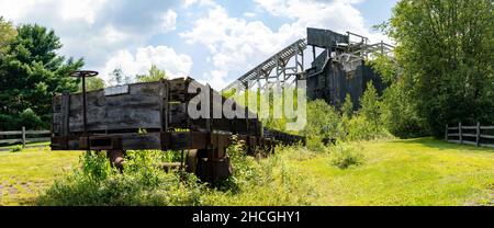 Ein historischer Kohlebrecher mit einem baufälligen hölzernen Eisenbahnwagen im Vordergrund. Stockfoto