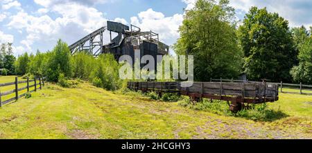 Ein historischer Kohlebrecher mit einem baufälligen hölzernen Eisenbahnwagen im Vordergrund. Stockfoto