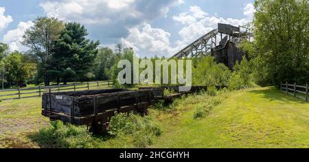 Ein historischer Kohlebrecher mit einem baufälligen hölzernen Eisenbahnwagen im Vordergrund. Stockfoto