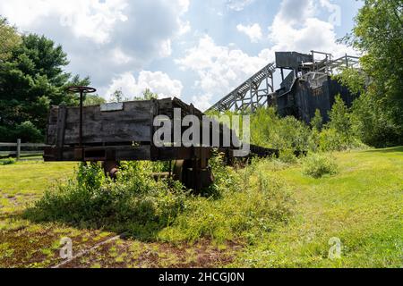 Ein historischer Kohlebrecher mit einem baufälligen Eisenbahnwagen im Vordergrund, der sich selektiv konzentriert. Stockfoto