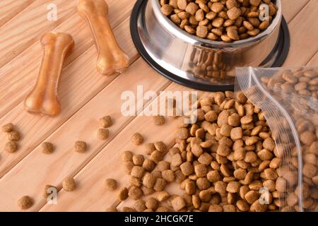 Hundekroketten in Säcken und Futterhäuschen auf Holztisch mit gepressten Hautknochen. Erhöhte Ansicht. Horizontale Zusammensetzung. Stockfoto