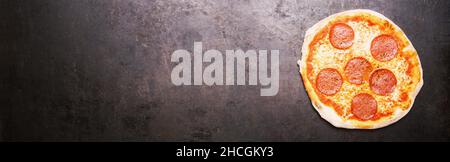 Leckere Salami-Pizza und Kochzutaten Tomaten Basilikum auf schwarzem rostigen Hintergrund. Draufsicht auf heiße Salami-Pizza, mit Copyspace für Ihren individuellen Stockfoto