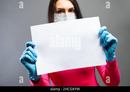 Frau in medizinischer Maske und Handschuhen, die leeres leeres leeres Papier in ihren Händen zeigt. Konzentrieren Sie sich auf ein Stück Papier. Verhindern Sie, dass andere von Corona COVID-19 und SARS COV 2 Stockfoto